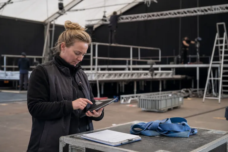 Aufbauleiterin prüft eine digitale Checkliste vor einer mobilen Bühne.