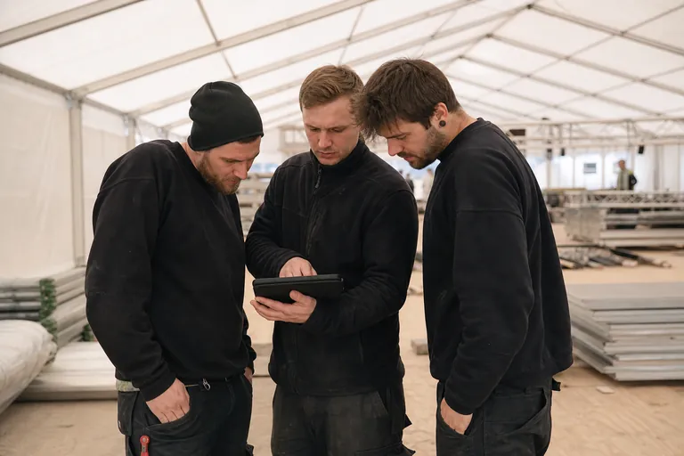 Montageteam ruft technische Unterlagen auf einem Tablet neben einem Veranstaltungszelt auf.